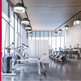 A spacious fitness gym lit by pendant lights with large windows and exercise equipment.